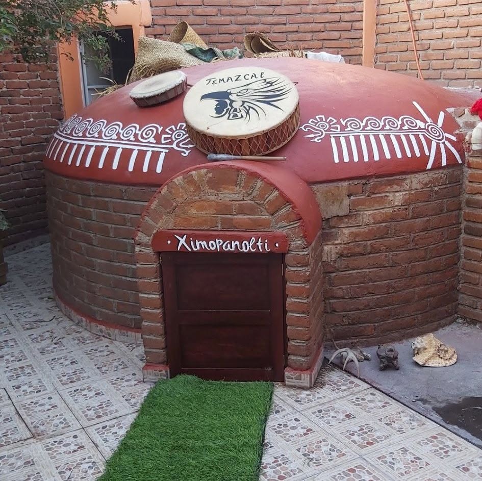 Temazcal tradicional de ladrillo con tambores ceremoniales y la palabra Ximopanolti sobre la puerta